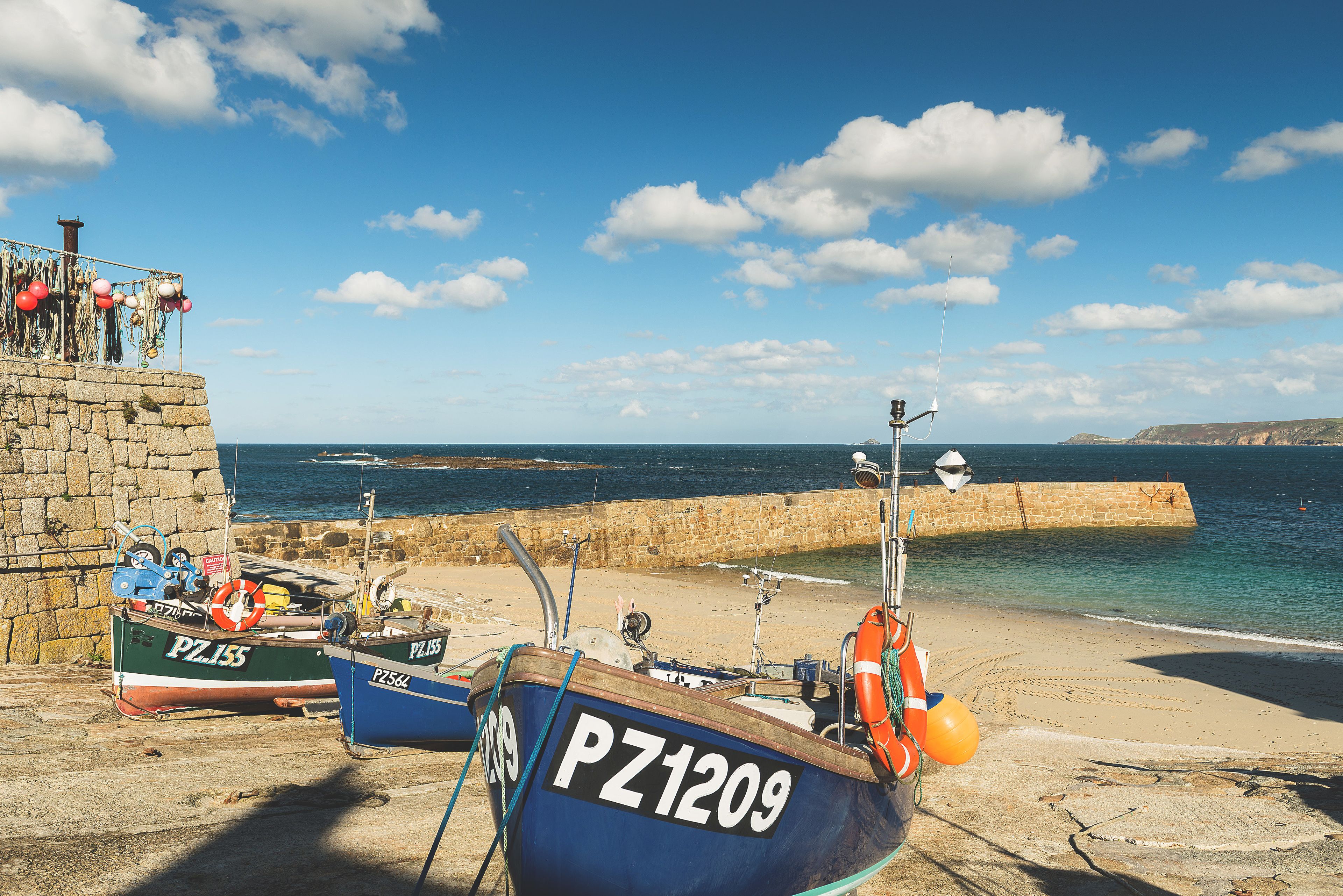 Boats docked at a stone pier with a clear view of the sea and a stone wall.