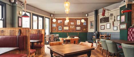 A restaurant interior with wooden flooring, multiple seating areas including booths and tables, hanging pendant lights, and framed pictures on the walls.