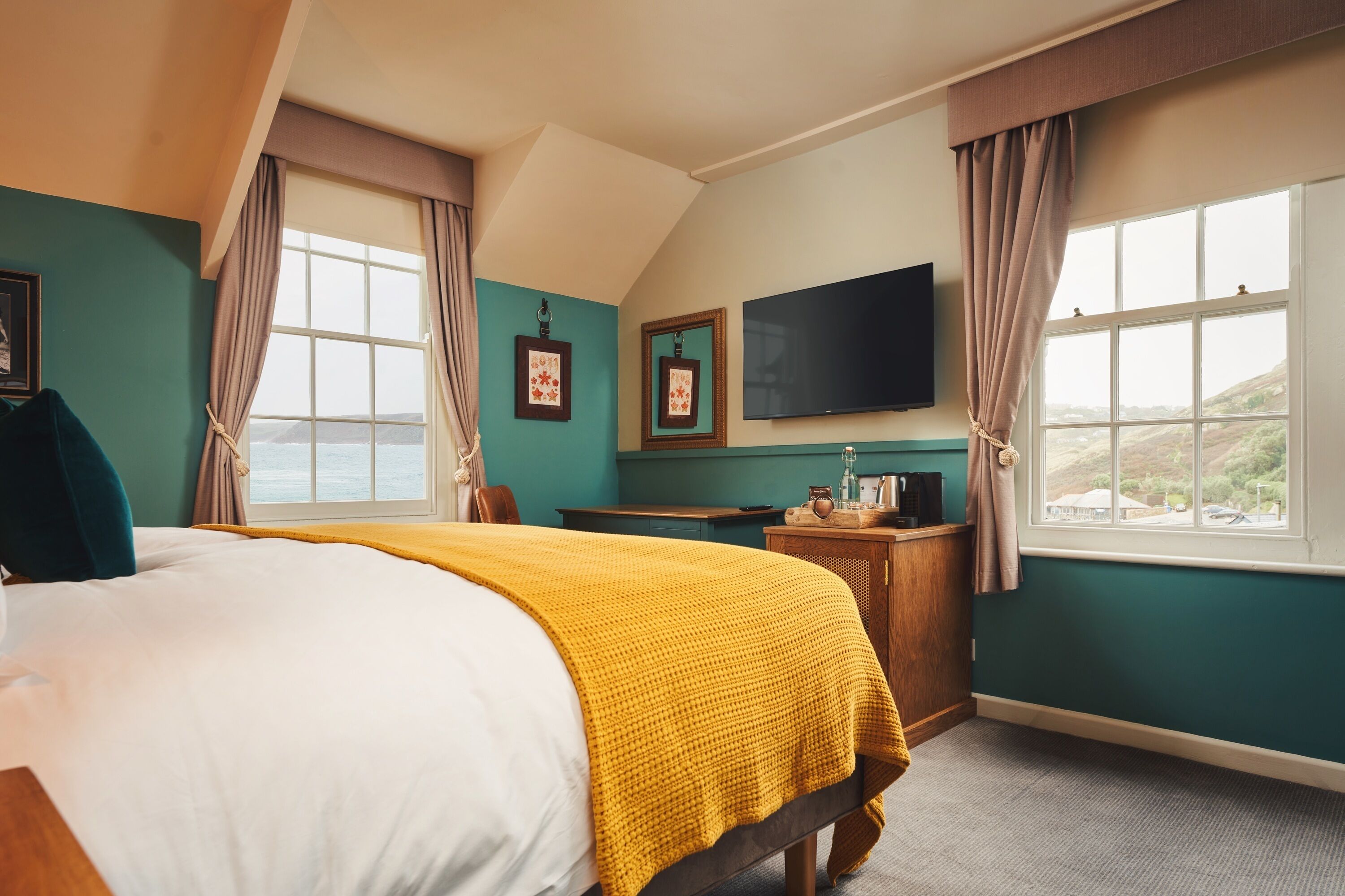 A hotel room with a large bed, a desk, a flat-screen TV, and a view of the sea.
