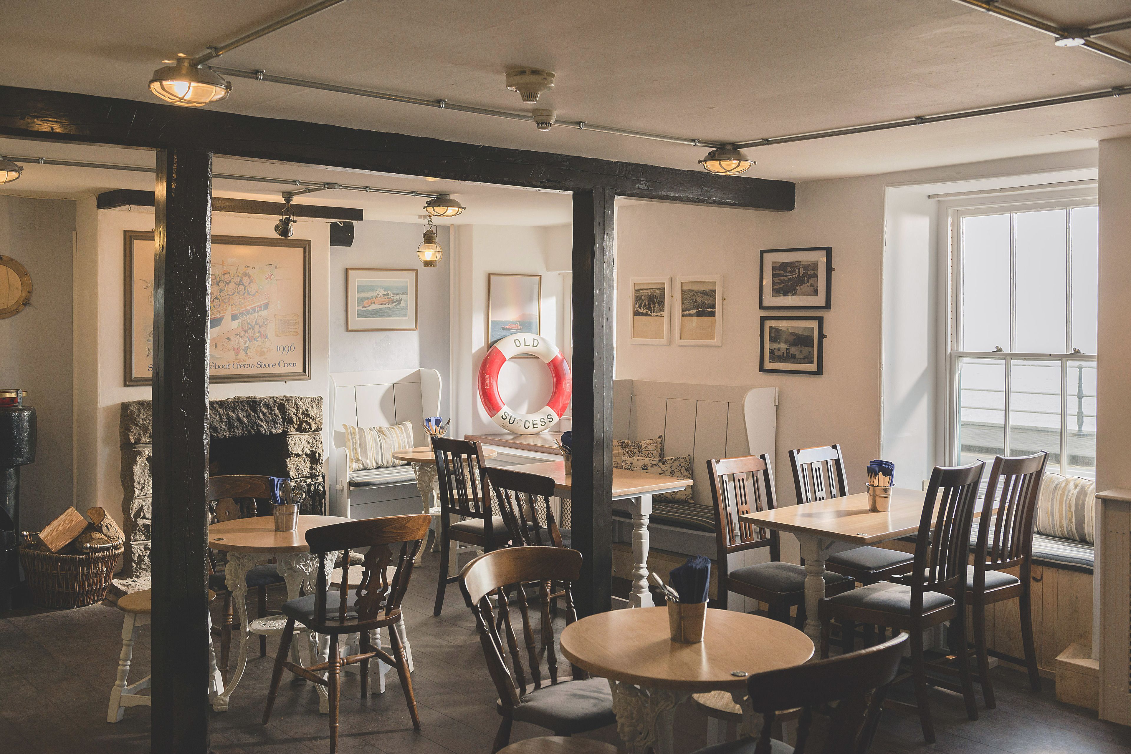 A cozy restaurant with wooden furniture, stone walls, and framed pictures on the walls.