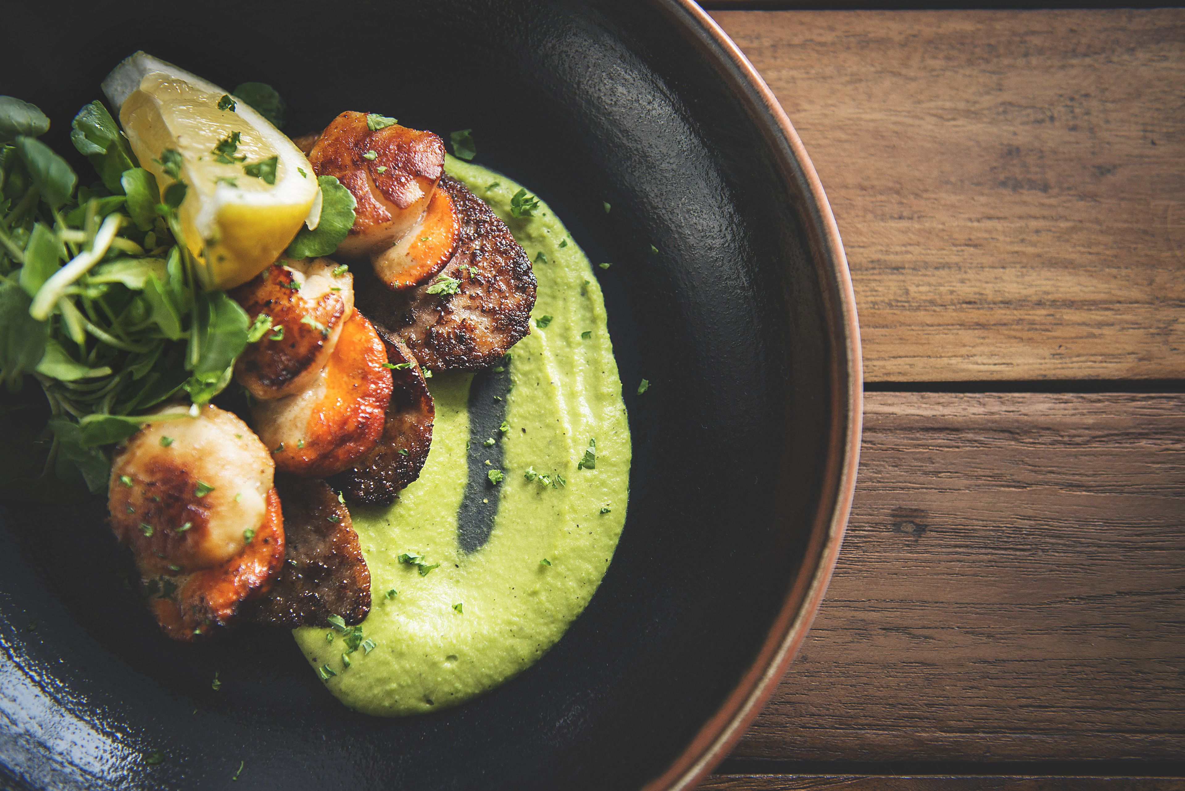 Un plato de comida con salsa verde, vegetales y rodajas de limón.