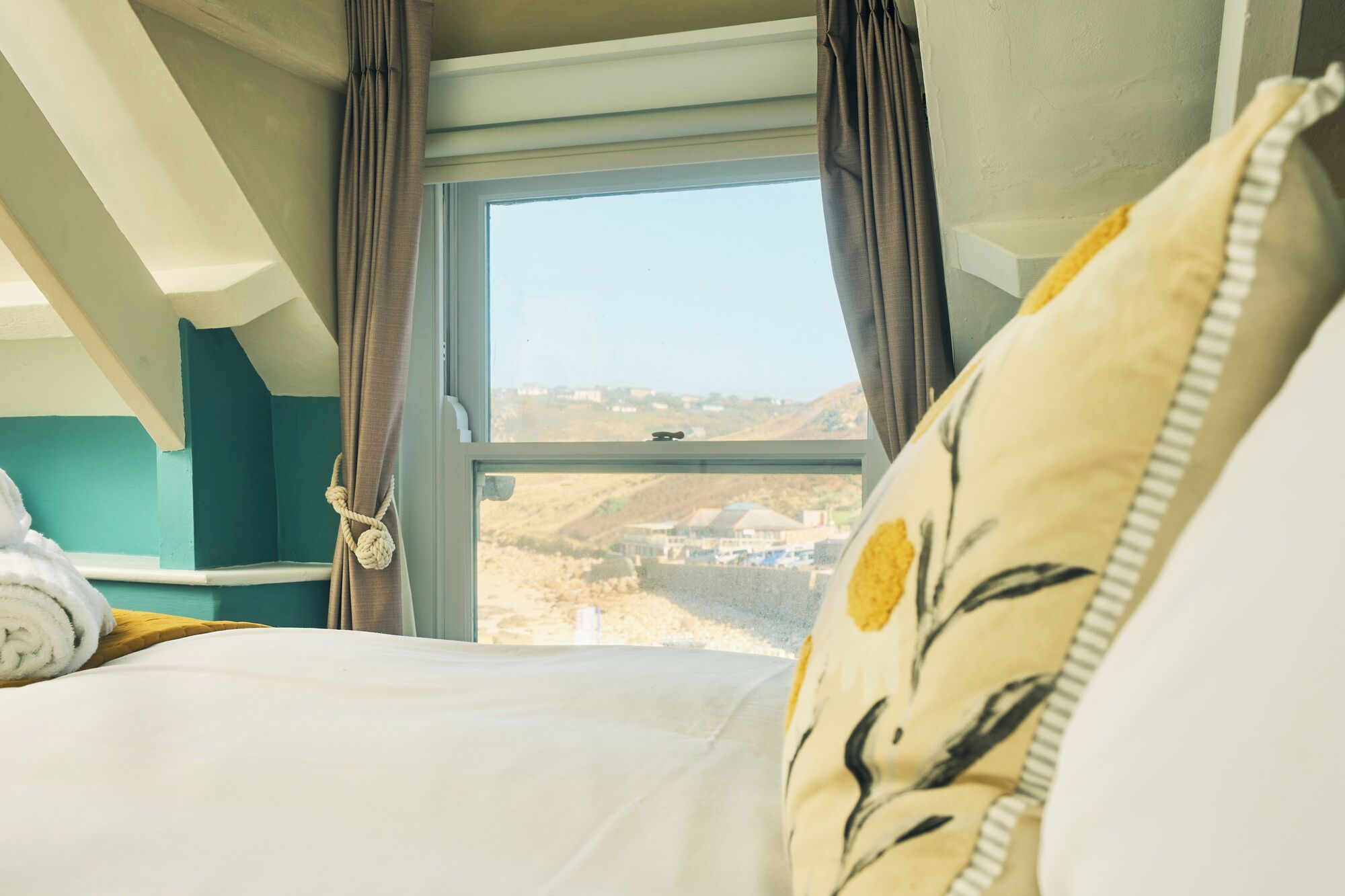 A bedroom with a large window, a bed with white bedding, and a view of a landscape.