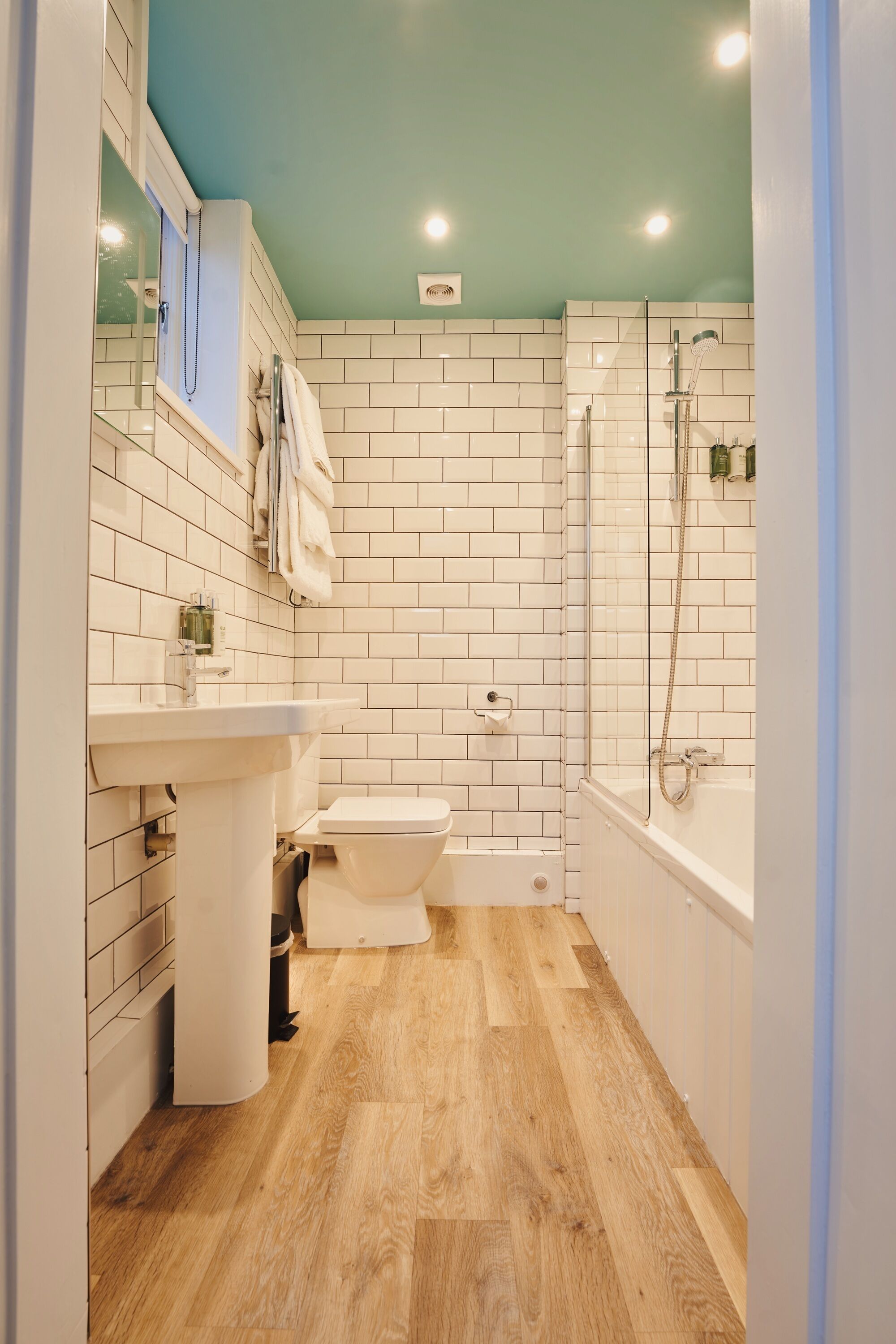 A bathroom with white tiled walls, a wooden floor, a toilet, a sink, a bathtub, and a shower.