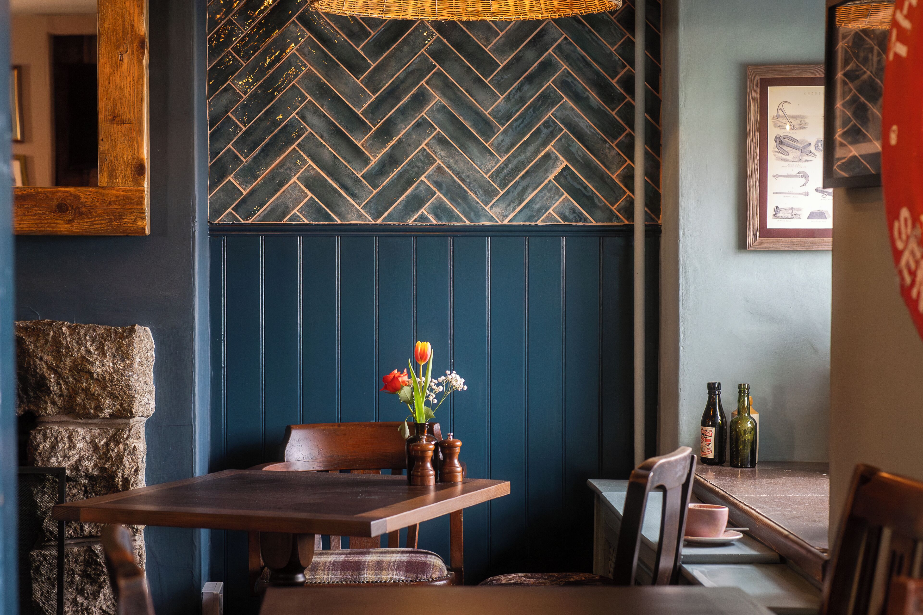 Un comedor con una mesa de madera, sillas y una pared con motivo de espiga. Hay dos botellas sobre la mesa y un florero con flores en la pared.