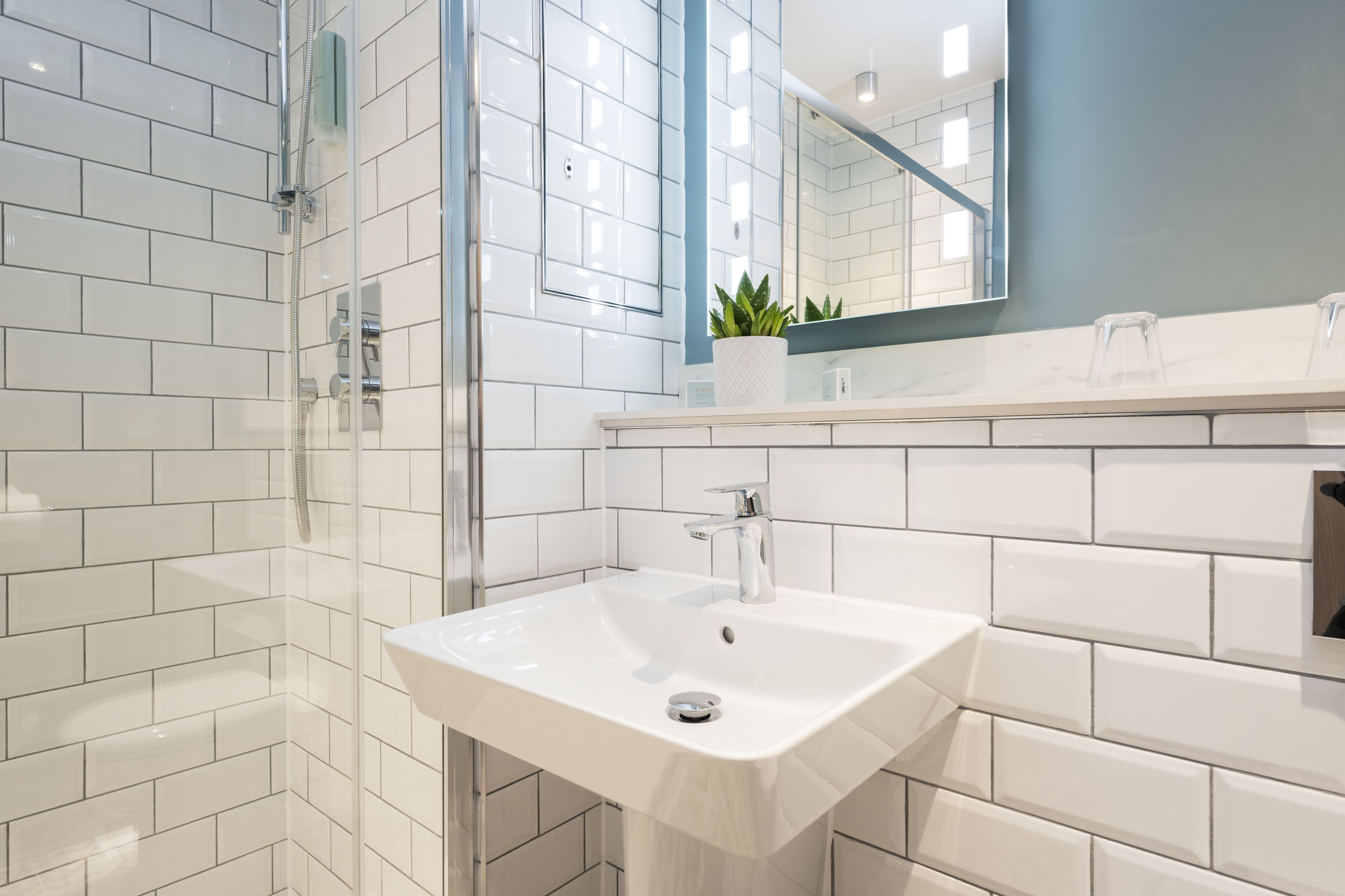 A modern bathroom with white subway tiles, a glass shower enclosure, a white sink, and a mirror above the sink.