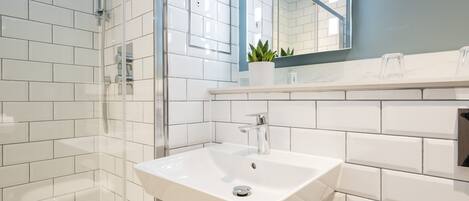 A modern bathroom with white subway tiles, a glass shower enclosure, a white sink, and a mirror above the sink.