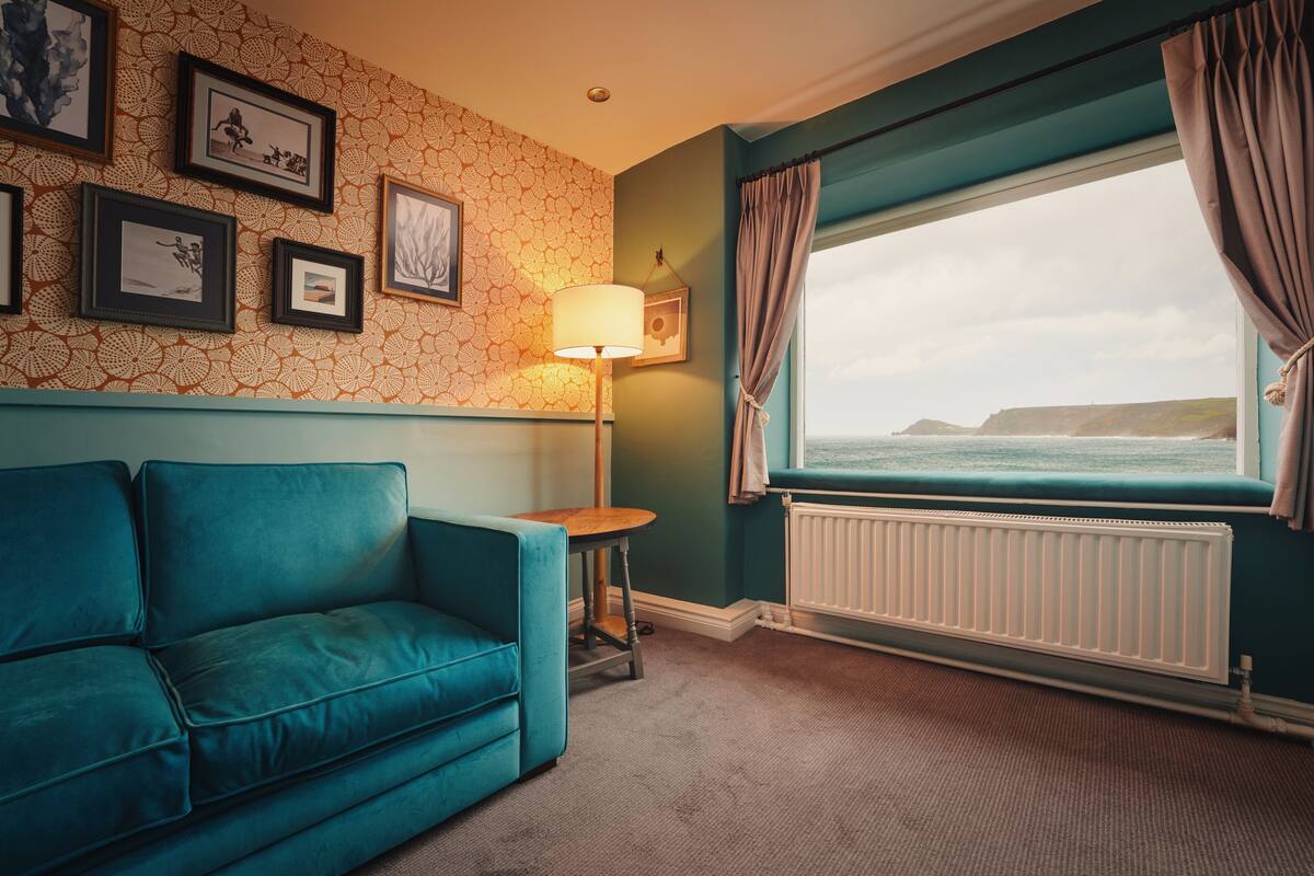 A teal-colored sofa, a small round table, a floor lamp, and a window with curtains.