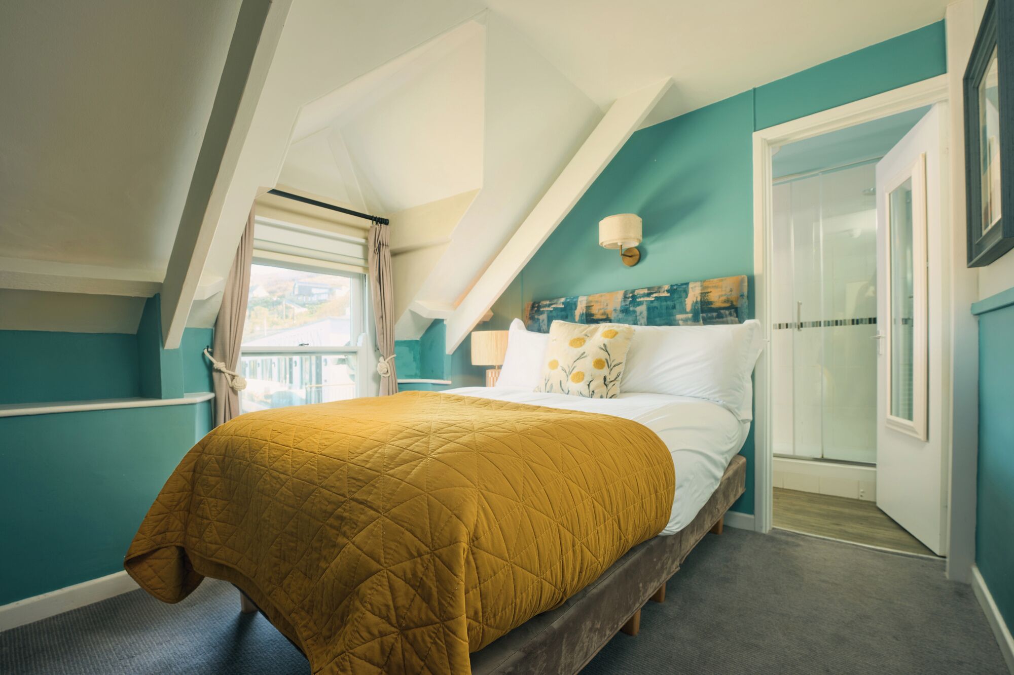 A bedroom with a bed, a window with curtains, a door, and a view of the outside.
