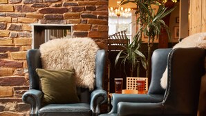 Two leather armchairs with fur throw pillows, a stone wall, and a potted plant. - Rashleigh Arms (St Austell)