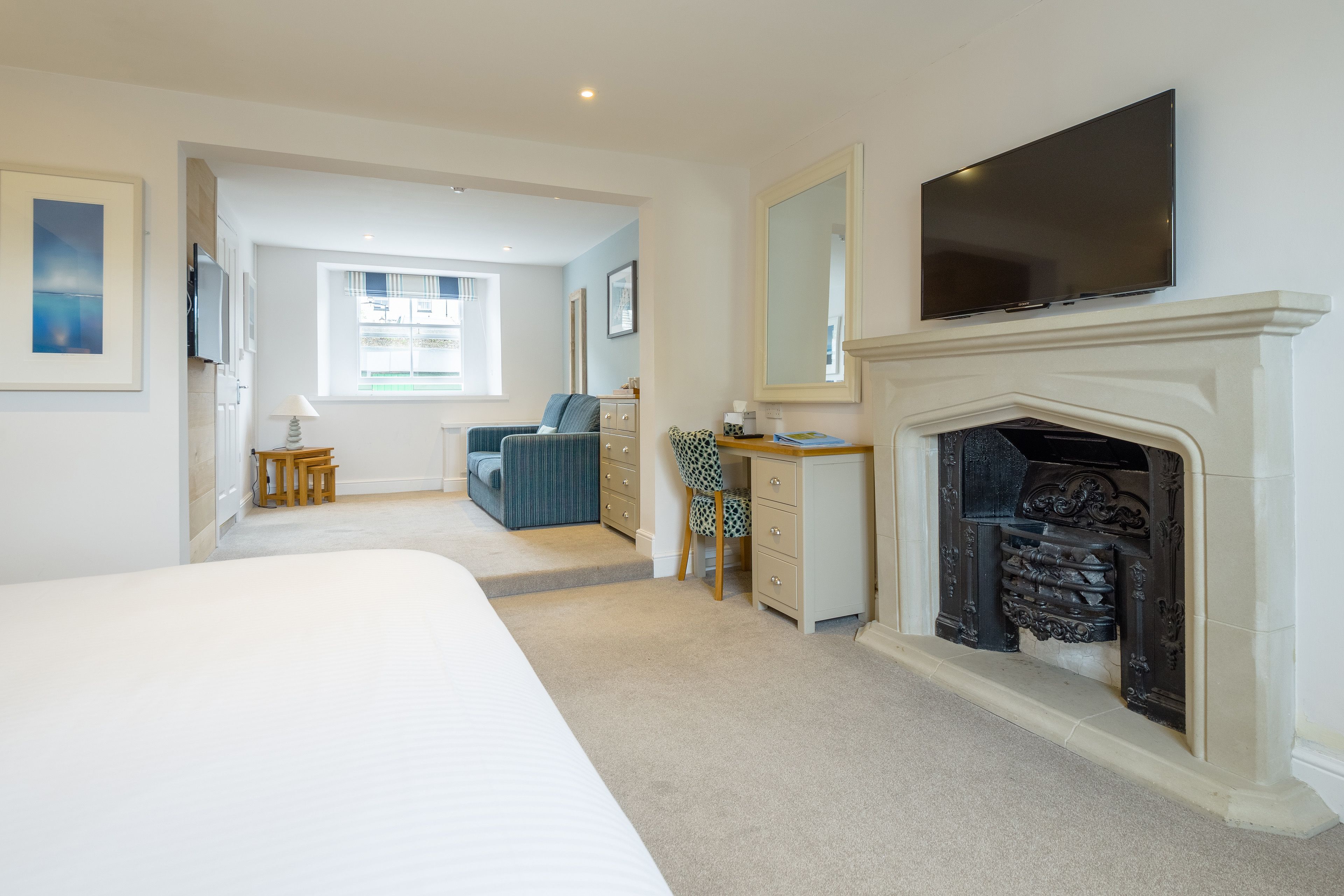 A bedroom with a large bed, a dresser, a desk, a television, and a fireplace.