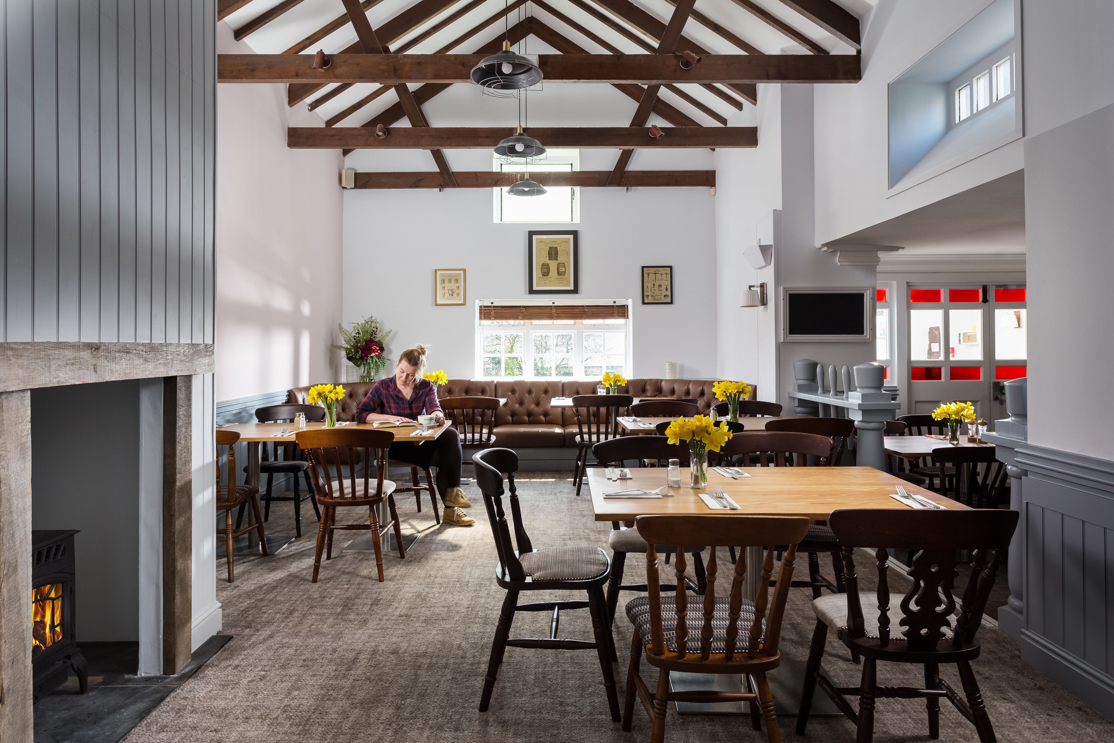 A spacious dining area with wooden tables and chairs, a fireplace, and a large window with natural light.