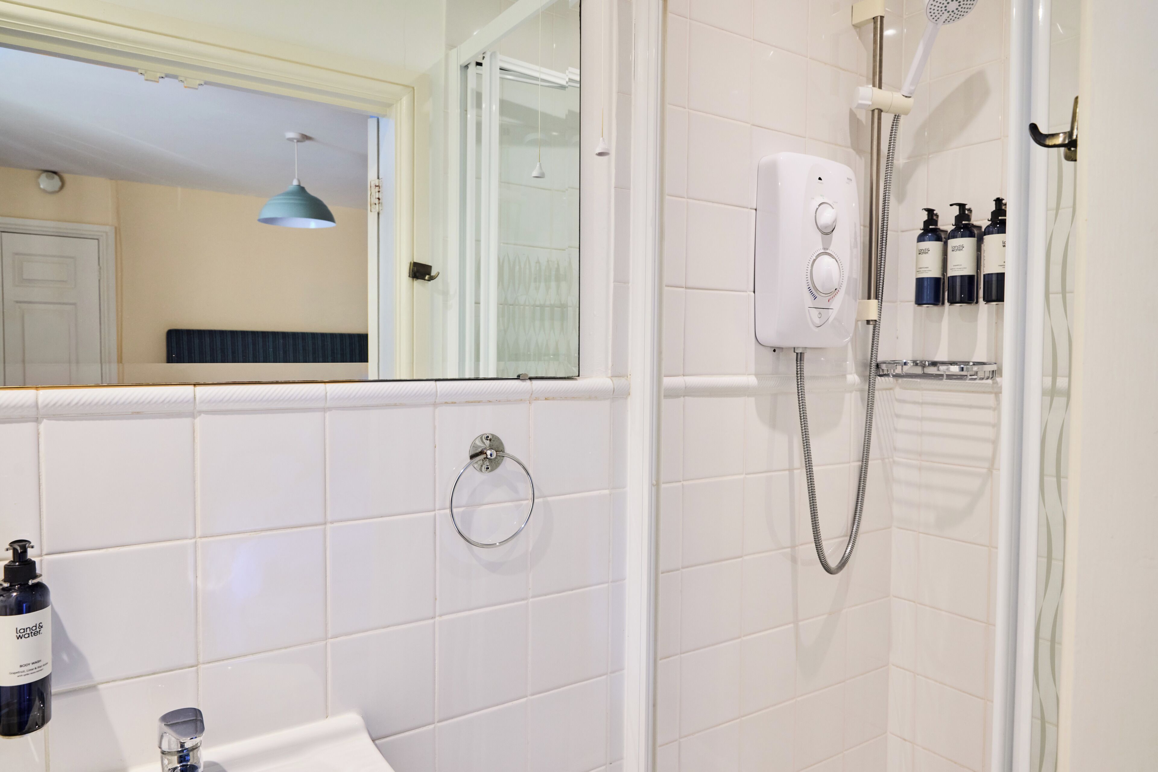 Un baño con ducha, toallero e lavamanos con jabón de cuerpo.