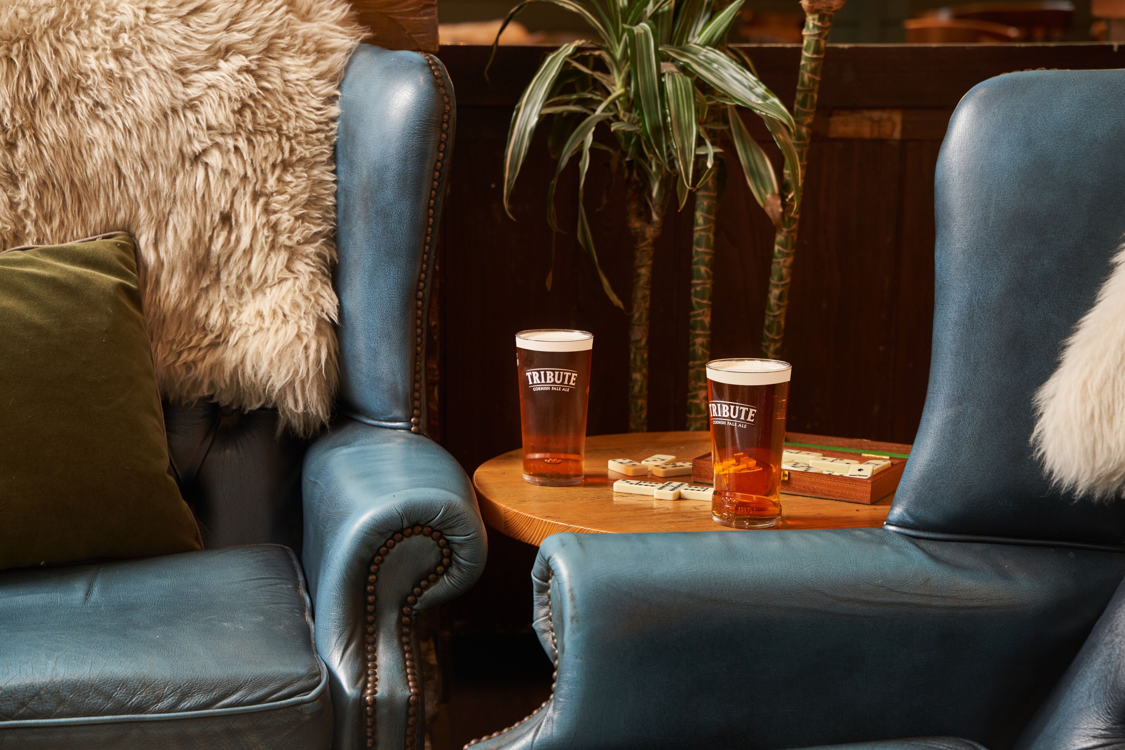 A seating area with two leather chairs, a small round table with two glasses of beer, and a plant in the background.