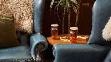 A seating area with two leather chairs, a small round table with two glasses of beer, and a plant in the background.