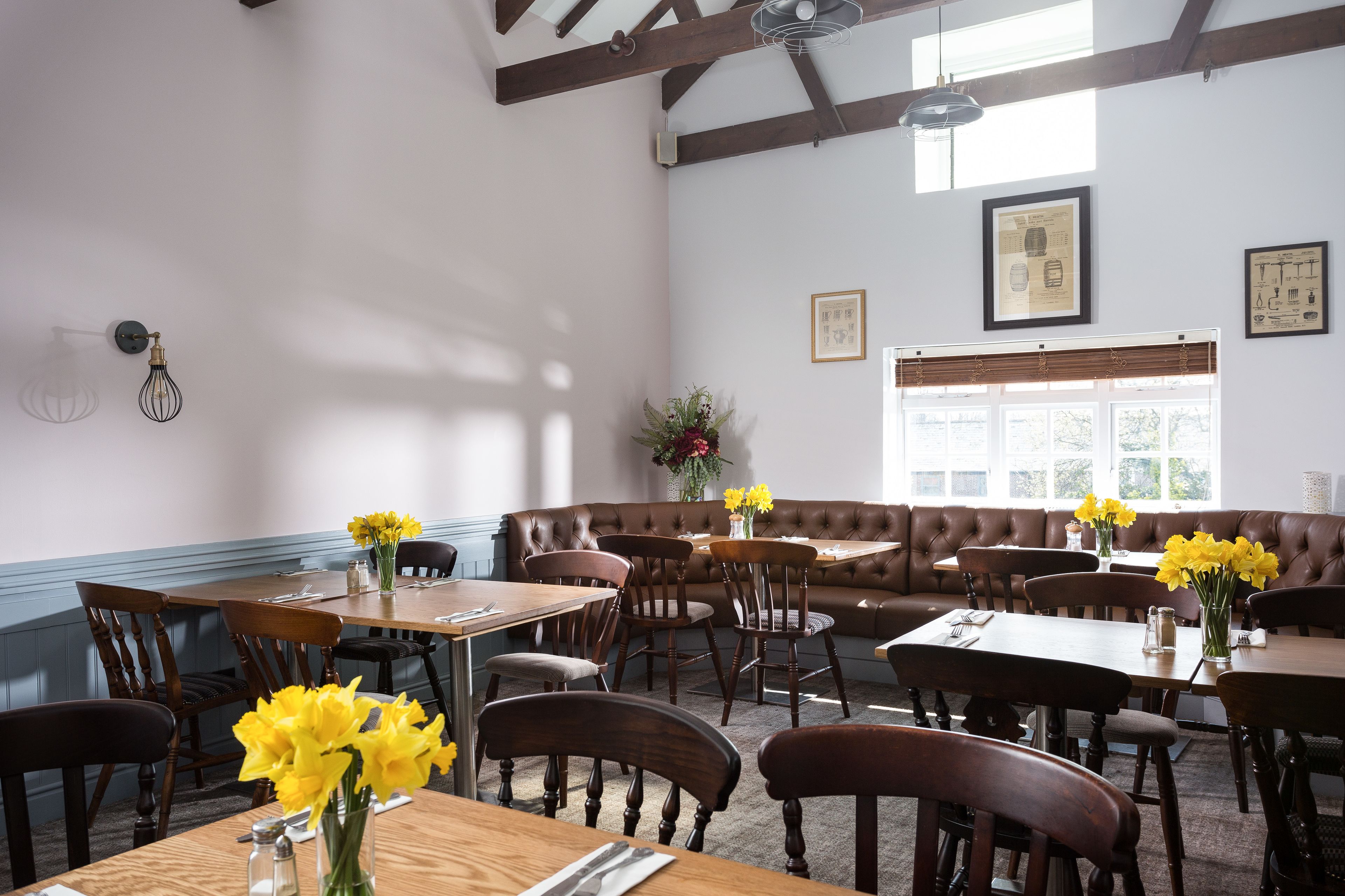 A dining area with wooden tables and chairs, a brown leather booth, and a window with blinds.