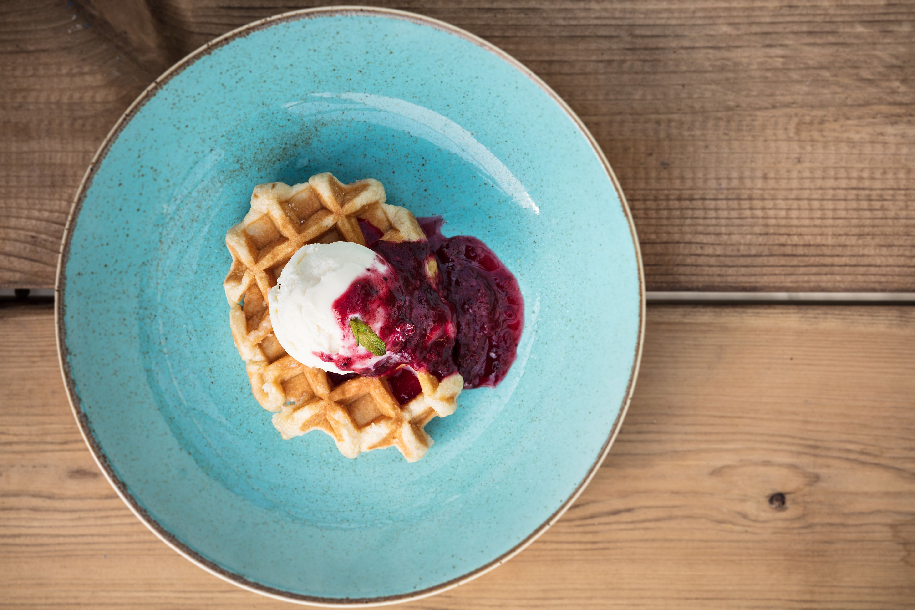 A plate with waffles, a scoop of ice cream, and a berry compote on a blue plate.