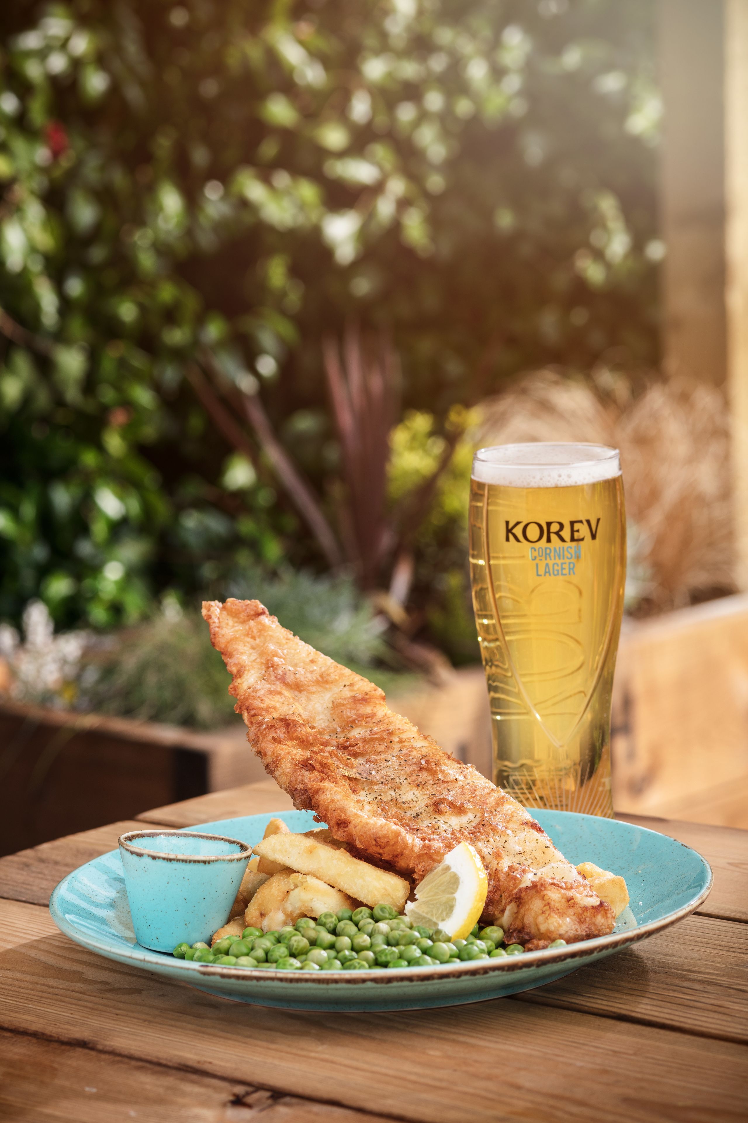 A plate of fish and chips with peas and a lemon wedge, accompanied by a tall glass of beer.
