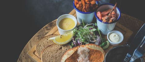 A wooden board with a variety of food items including bread, a salad, and a cup of shrimp.