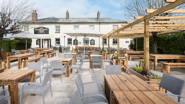 A pub with outdoor seating, wooden tables, wicker chairs, and a pergola. - Rashleigh Arms (St Austell)