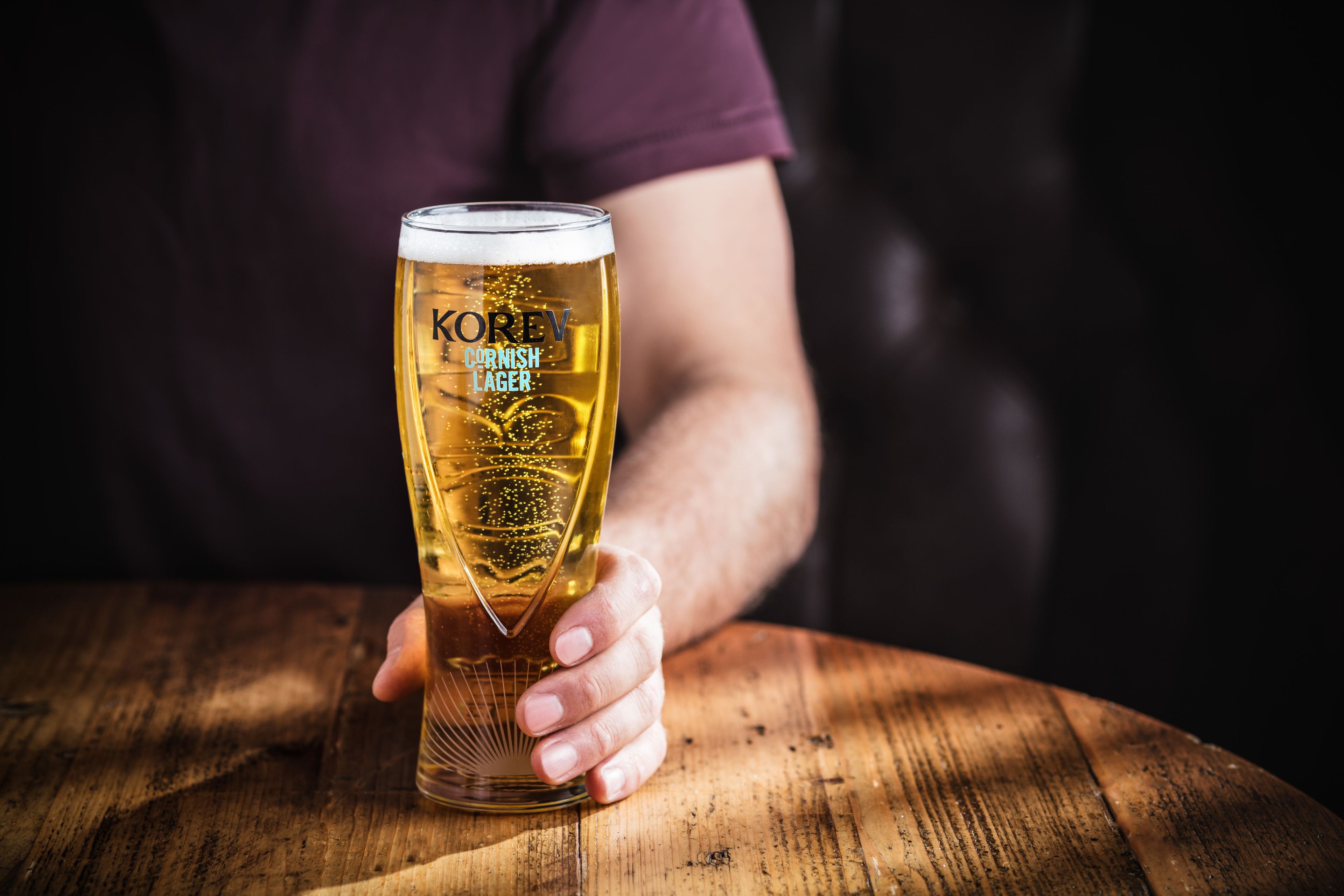 A person holding a tall glass of beer with a label that reads "KOREV German Lager."