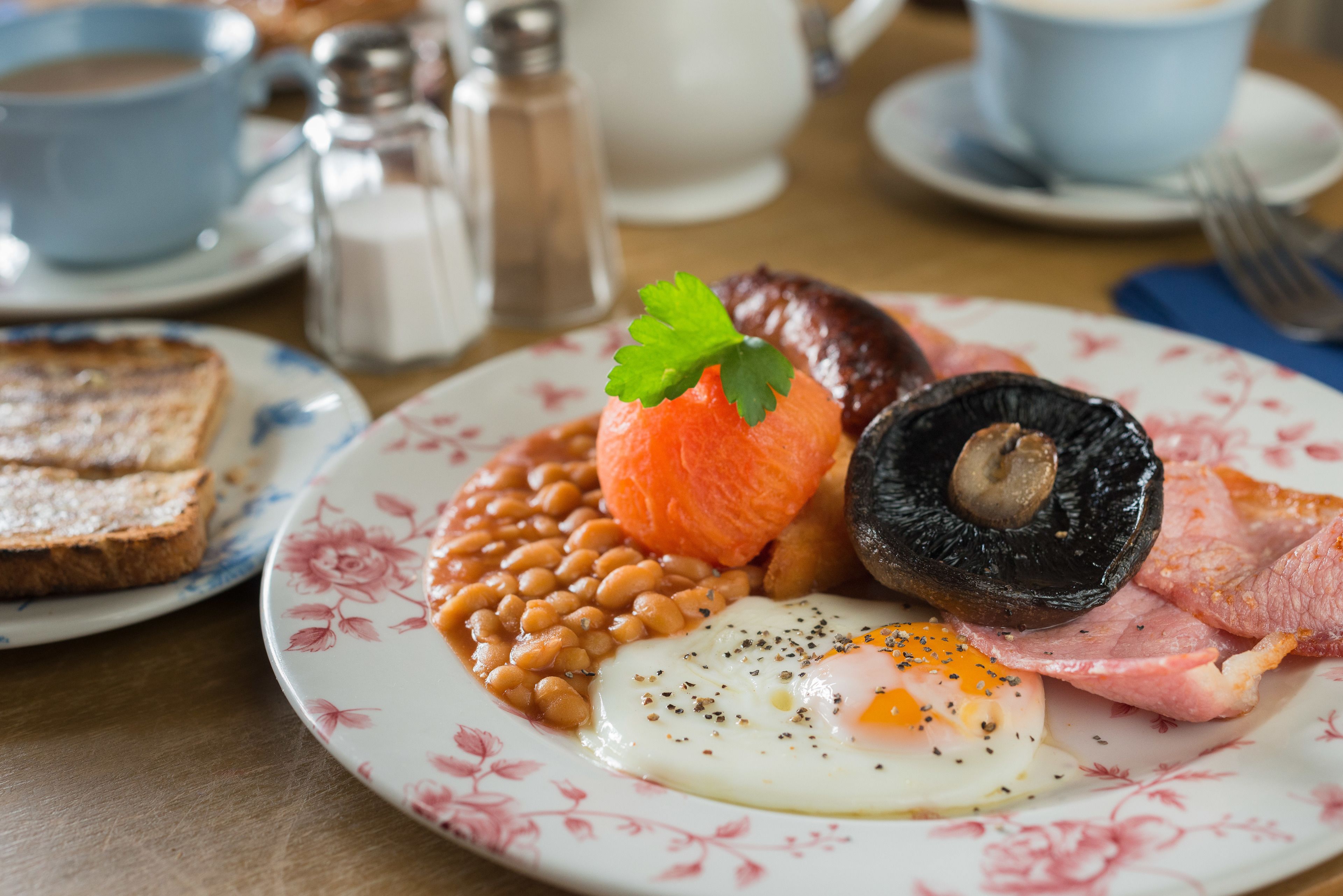 Un plato de comida para el desayuno con huevos, frijoles, tocino y un tomate a la plancha.