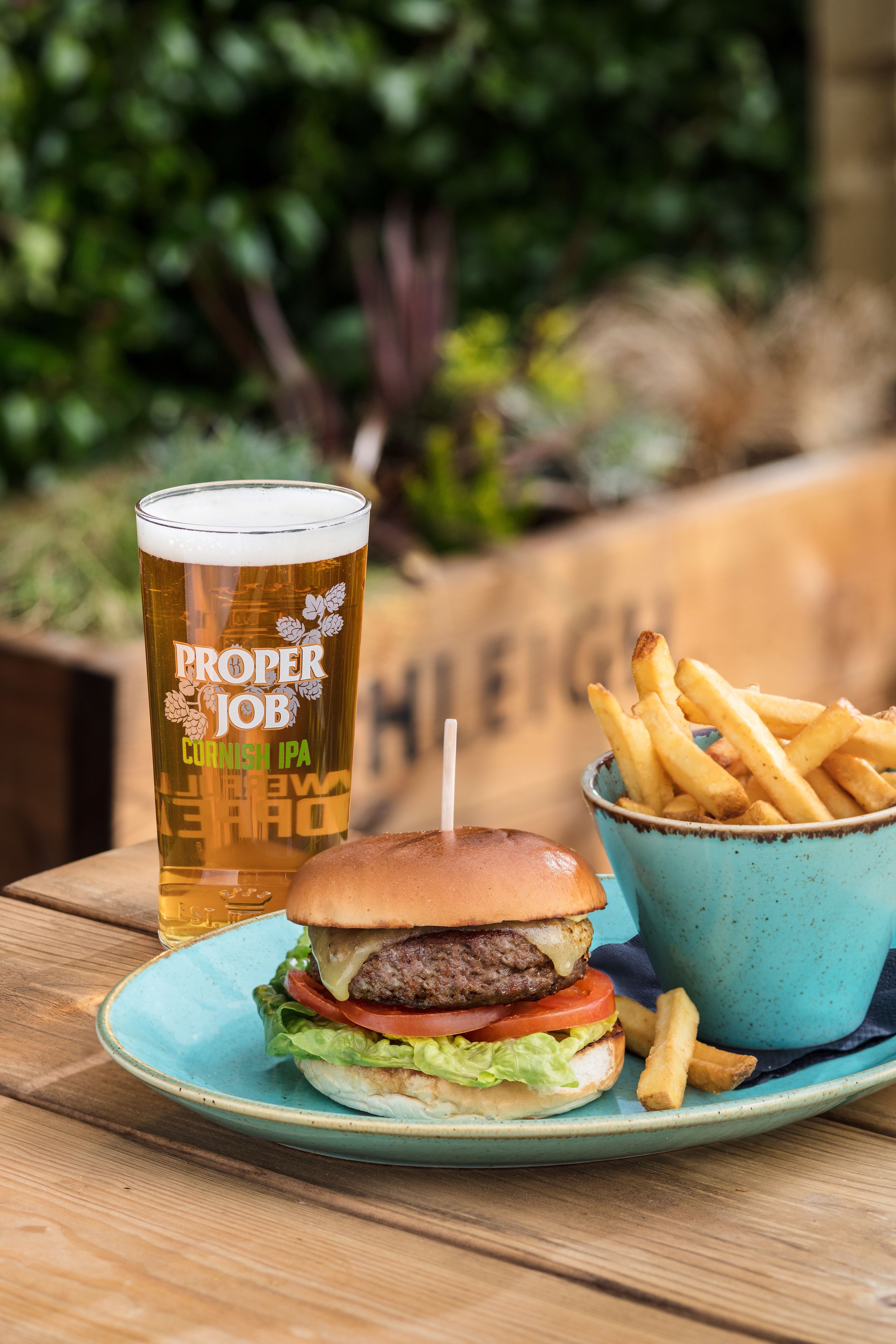 A meal consisting of a burger, fries, and a glass of beer on a wooden table.
