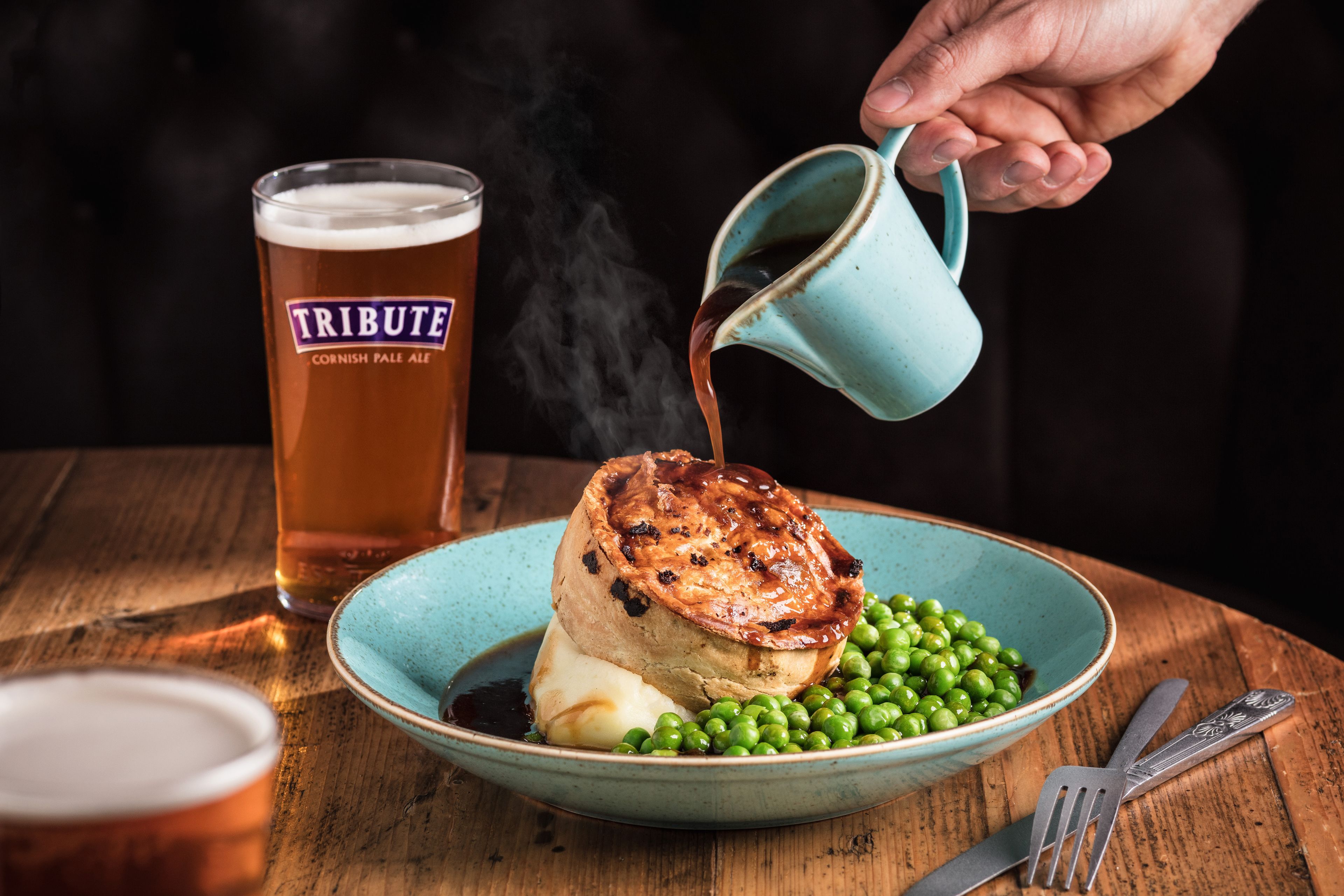 A meal with a meat pie, peas, and a glass of beer on a wooden table.