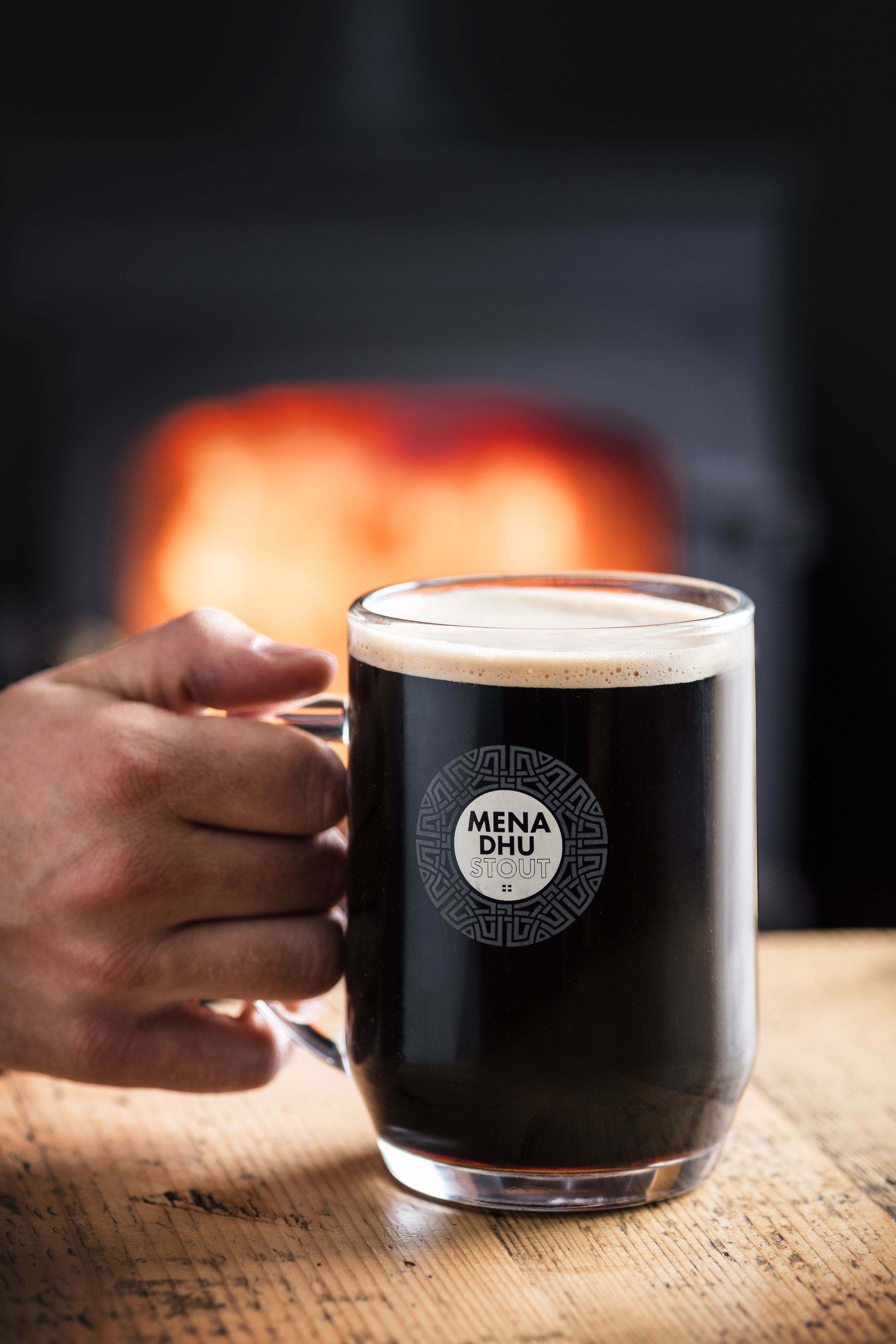 Una mano sosteniendo una taza con un logotipo, sobre una superficie de madera.