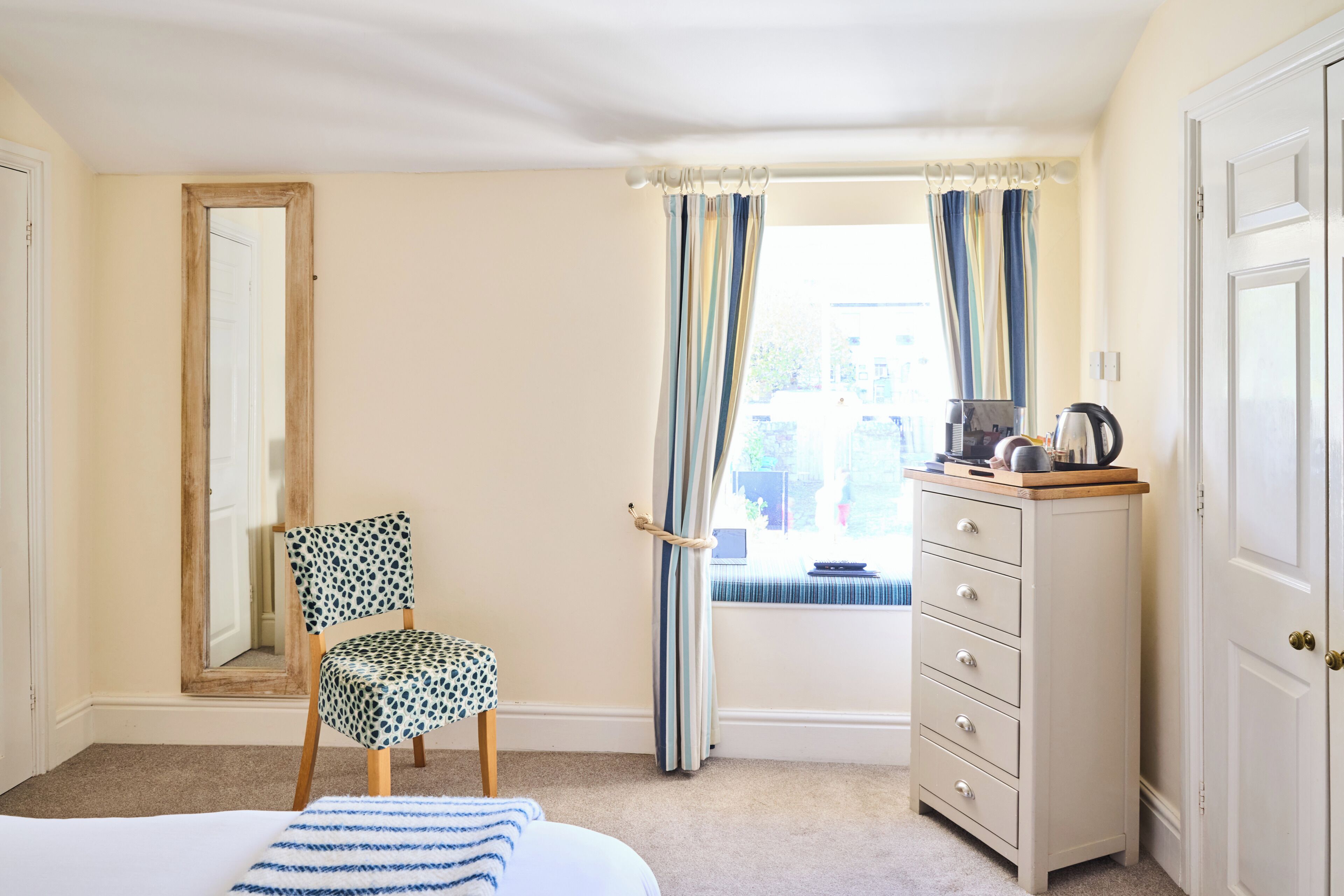 A bedroom with a bed, a chair, a dresser, a mirror, and a window with curtains.