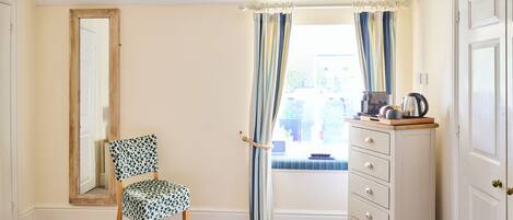 A bedroom with a bed, a chair, a dresser, a mirror, and a window with curtains.