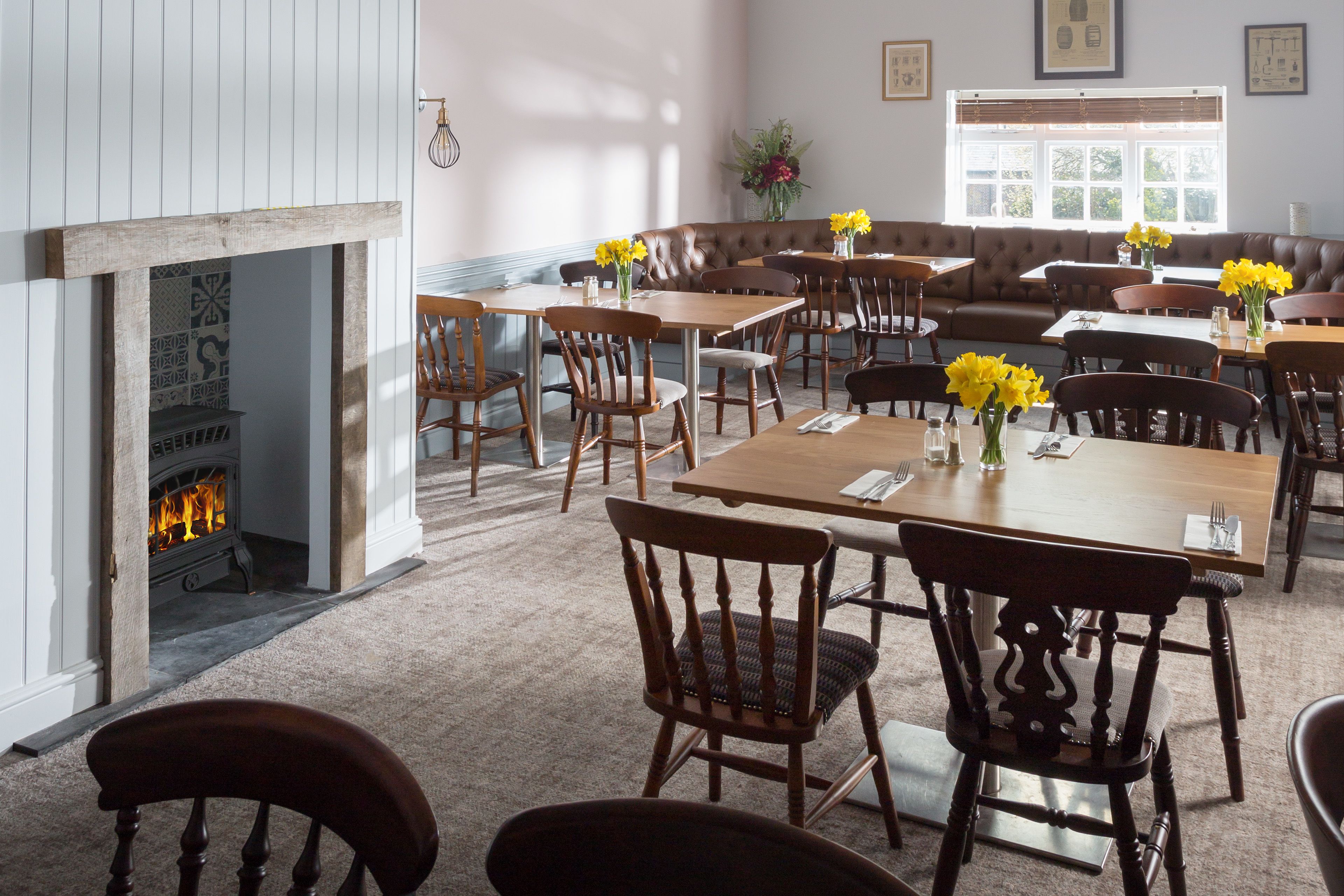 A cozy dining area with wooden tables and chairs, a fireplace, and a large window with natural light.