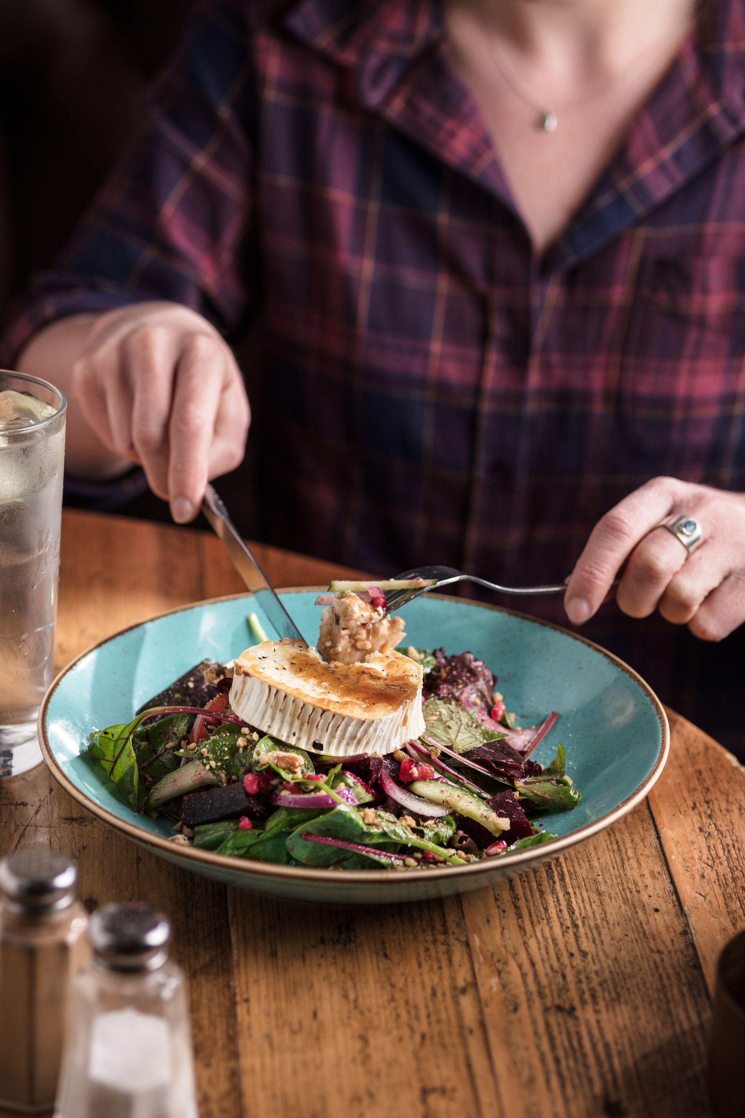 A person dining at a table with a plate of food, a glass of water, and salt and pepper shakers.