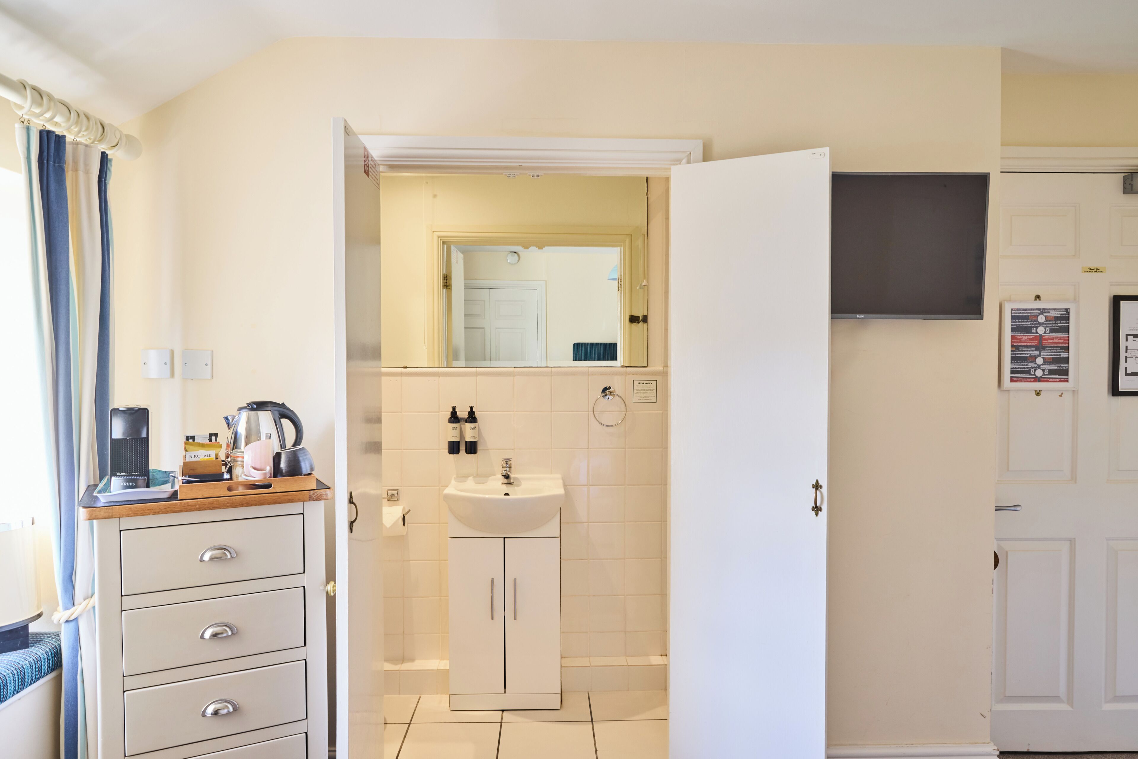 A hotel room with a kitchenette, a sink, a mirror, and a television.