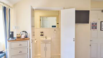 A hotel room with a kitchenette, a sink, a mirror, and a television.