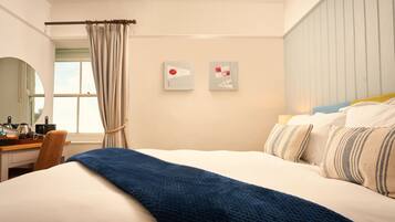 Ein Hotelzimmer mit einem Bett, einem Schreibtisch, einem Sessel, einem Fenster mit Vorhängen und zwei Wandbildern.