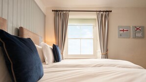 A bedroom with a large bed, a headboard, and a window with curtains. There are two wall-mounted pictures. - Rashleigh Arms (St Austell)