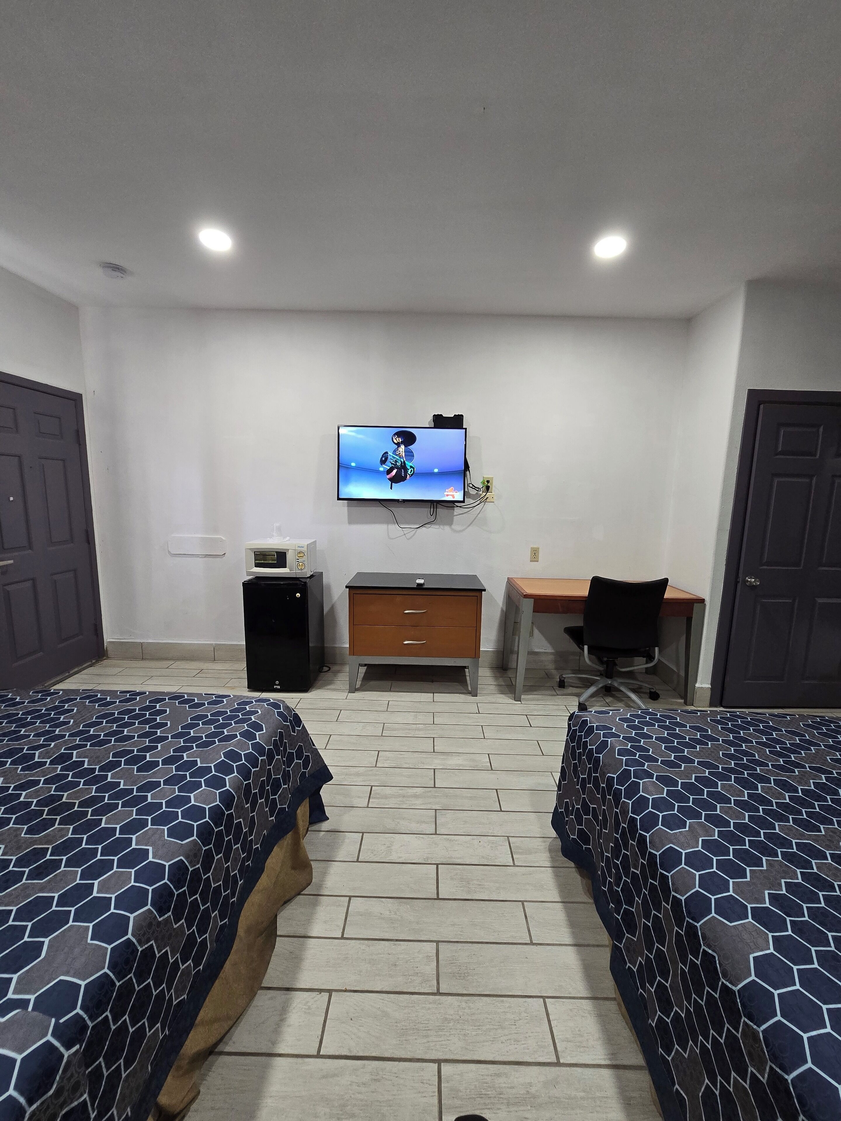 A hotel room with two beds, a desk, a chair, a TV on the wall, and a small cabinet.
