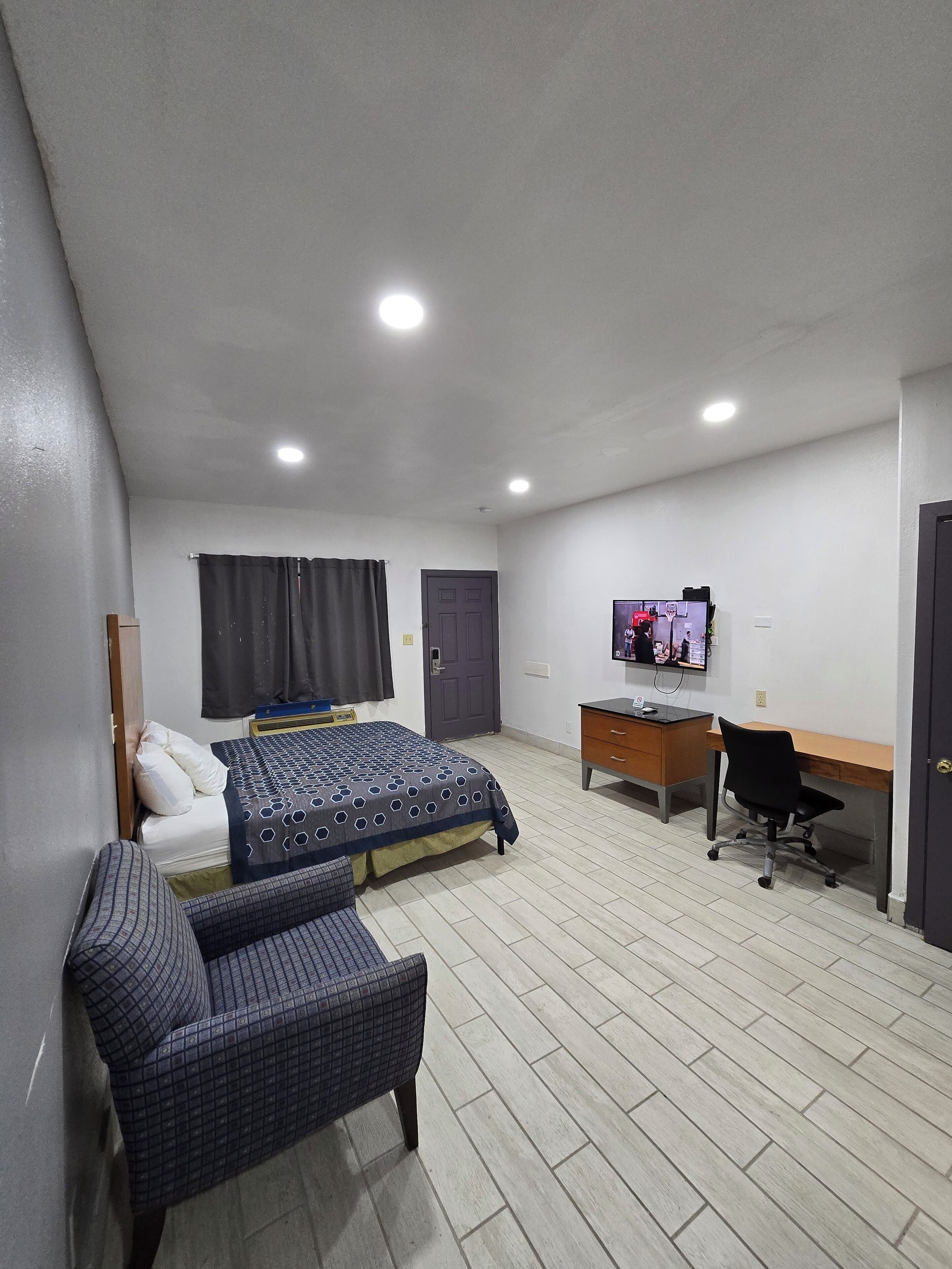 A bedroom with a bed, a desk, a chair, a television, and a wardrobe.