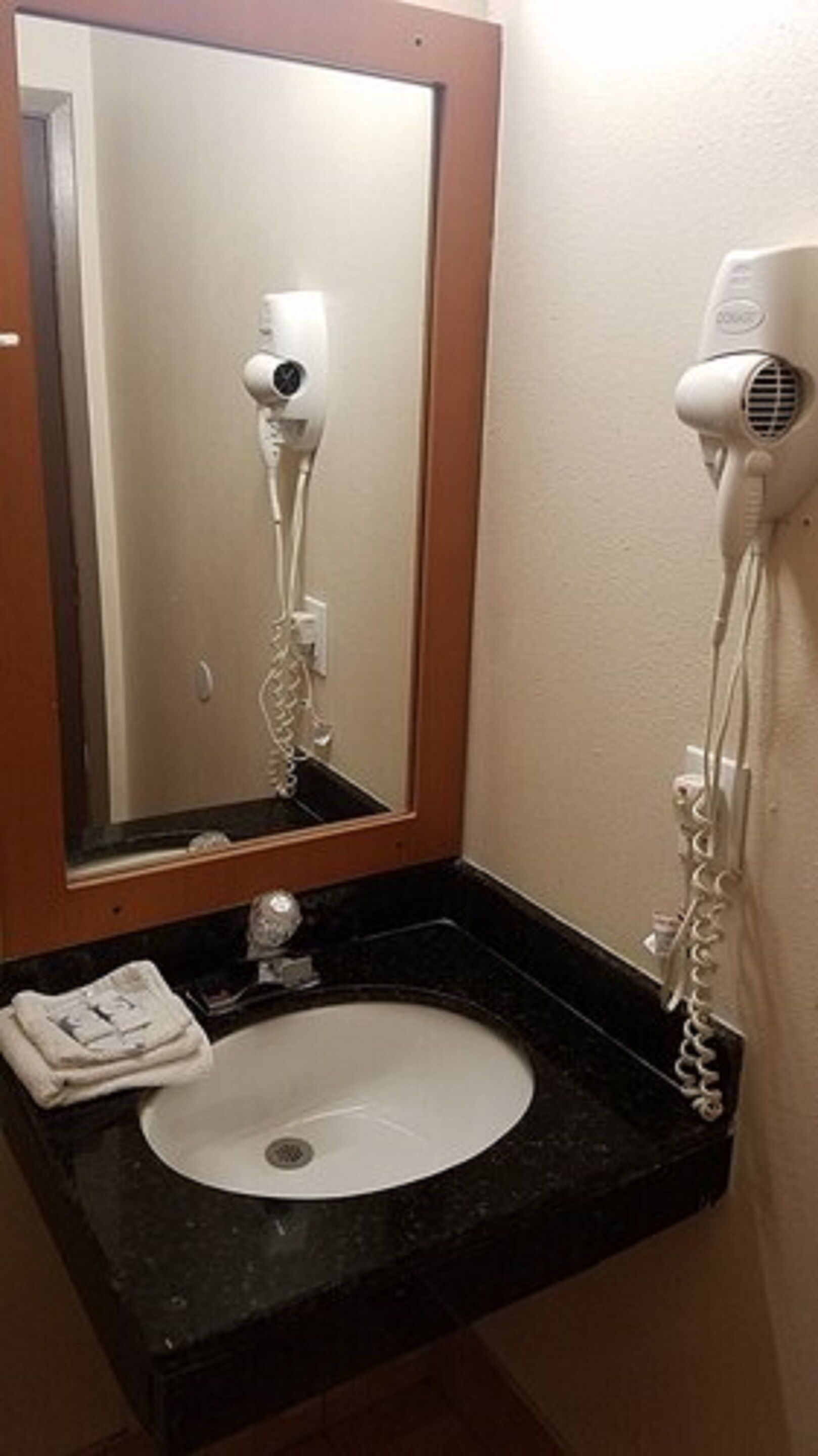 A bathroom with a white sink, a mirror with a wooden frame, and a hairdryer mounted on the wall.