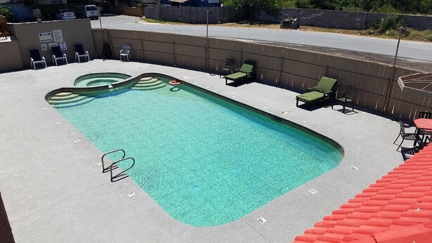 A rectangular swimming pool with a green and white wave design, surrounded by lounge chairs and a concrete deck. - Executive Inn and Suites (Port Isabel)