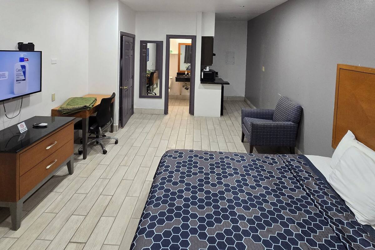 A hotel room with a bed, a desk, a chair, a TV, and a bathroom visible through an open door.