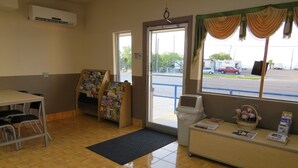 A reception area with a desk, chairs, a bulletin board, a trash bin, and a window with a view of the parking lot. - Executive Inn and Suites (Port Isabel)