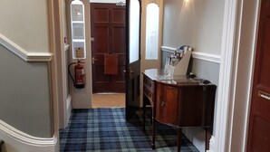 A hallway with a checkered carpet, a wooden desk with a lamp, and a door with a fire extinguisher. - Kingswood (Stockton-on-Tees)
