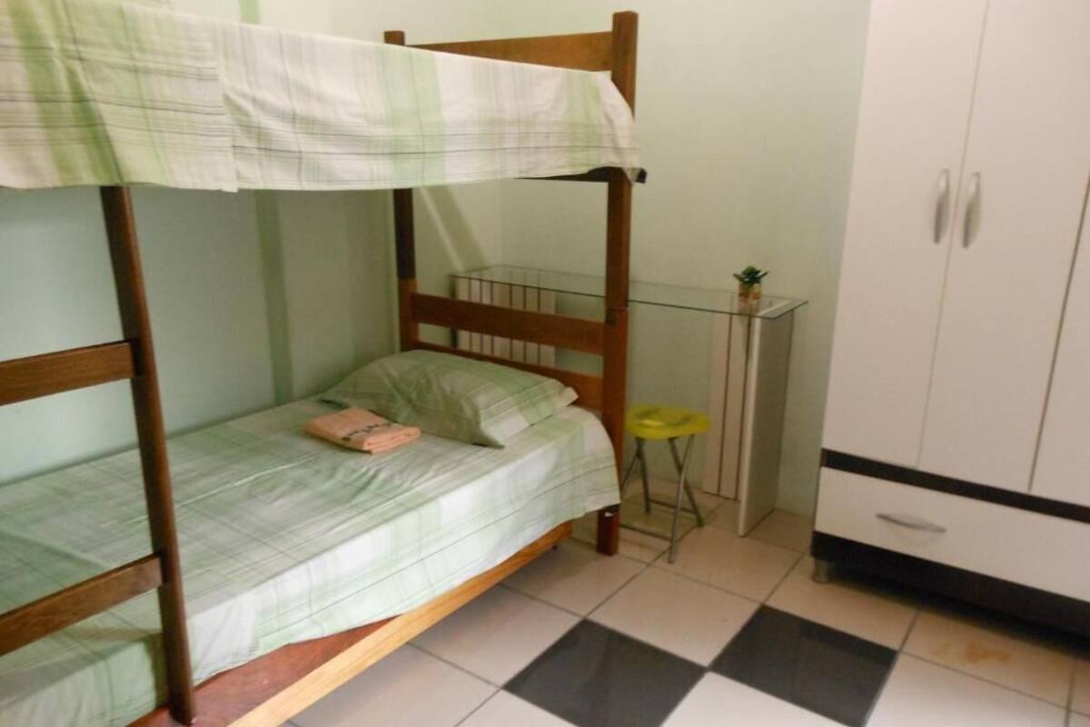 A single-occupancy room with a bunk bed, a small stool, a cabinet, and a tiled floor.