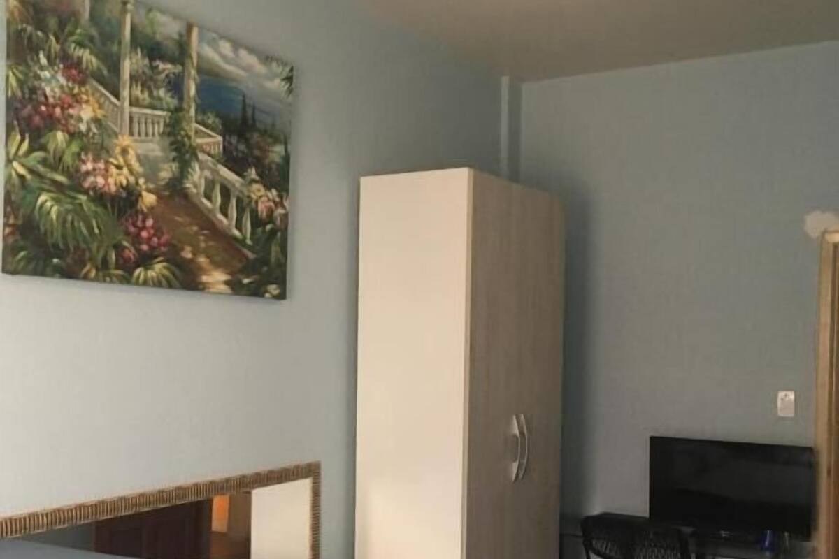 A bedroom with a bed, a wardrobe, a desk with a chair, and a ceiling fan.