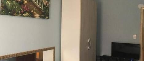 A bedroom with a bed, a wardrobe, a desk with a chair, and a ceiling fan.