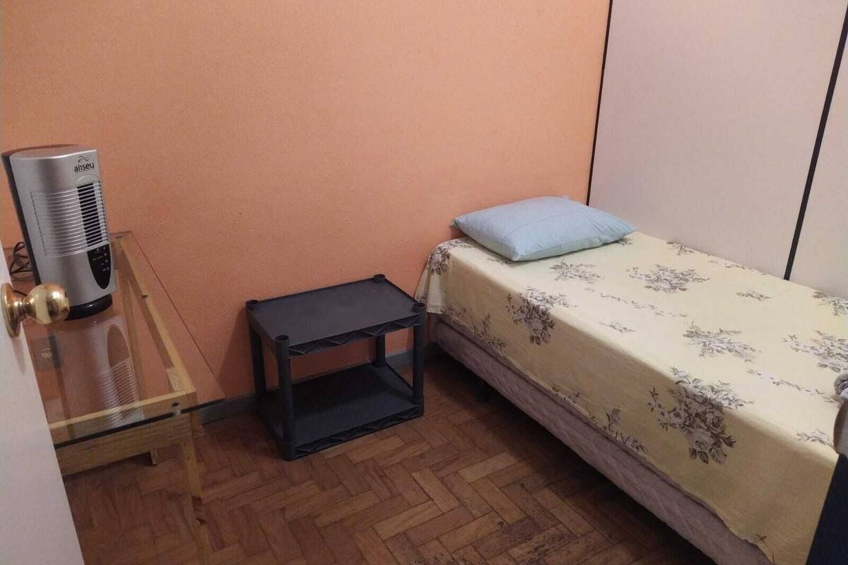 A small room with a bed, a bedside table, a heater, and a wardrobe.
