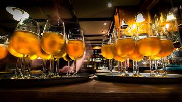 Um bar com vários copos de cerveja em bandejas, uma pessoa ao fundo e prateleiras com garrafas.