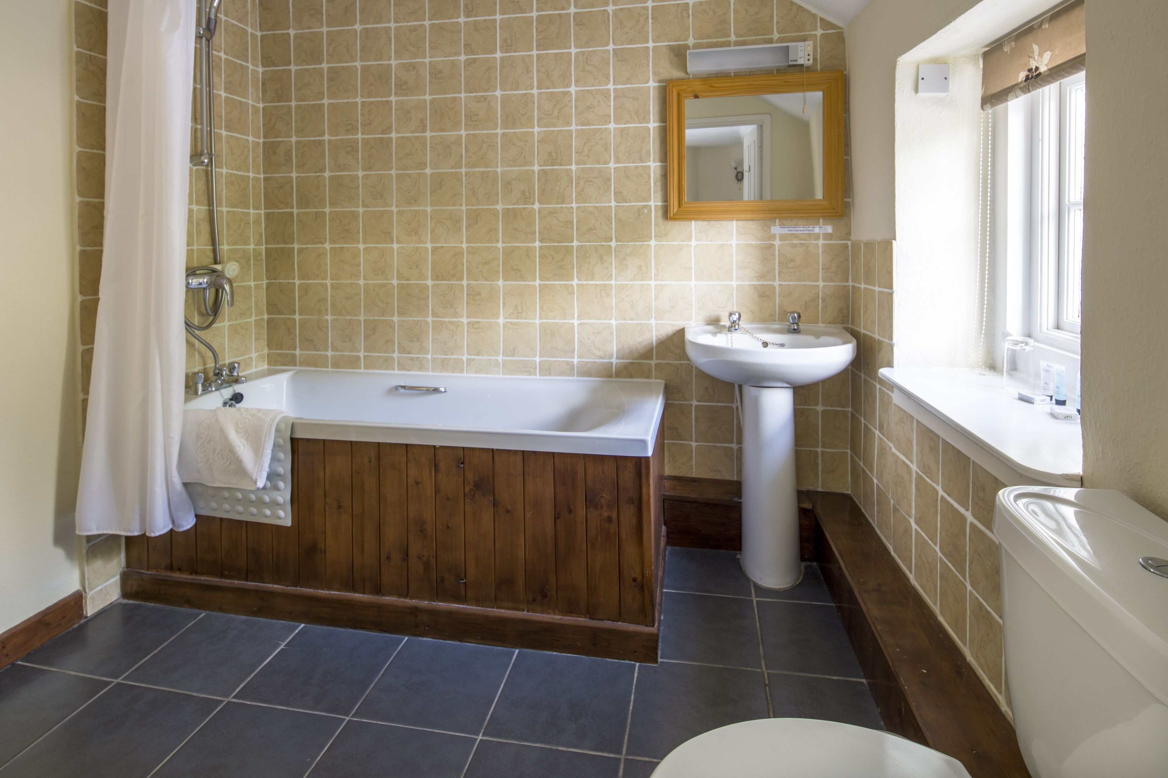 A bathroom with a wooden bathtub, a white sink, and a window.