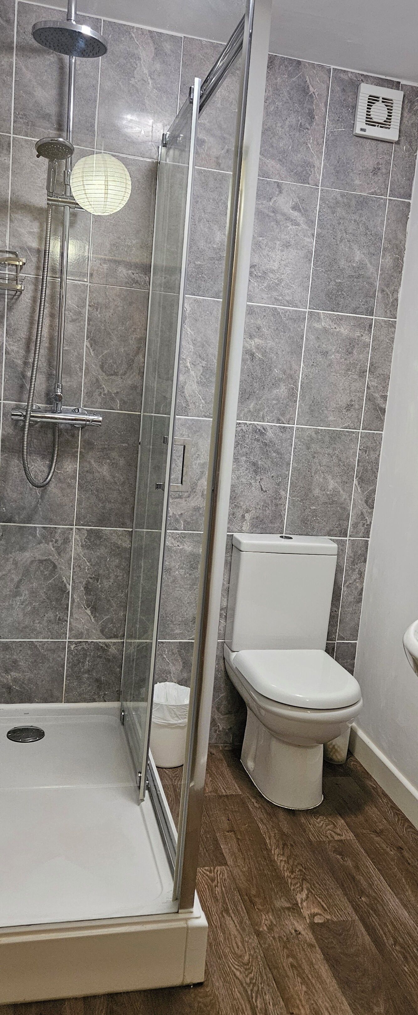 A bathroom with a glass-enclosed shower, a white toilet, and grey marble tiles.